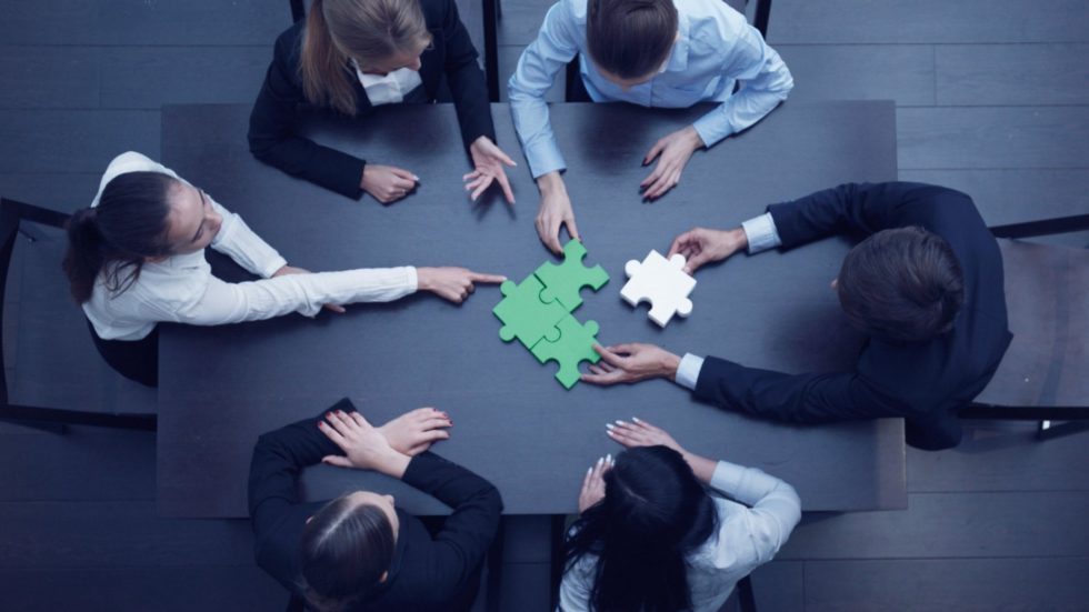 Six employees fitting a white puzzle piece into a set of green ones