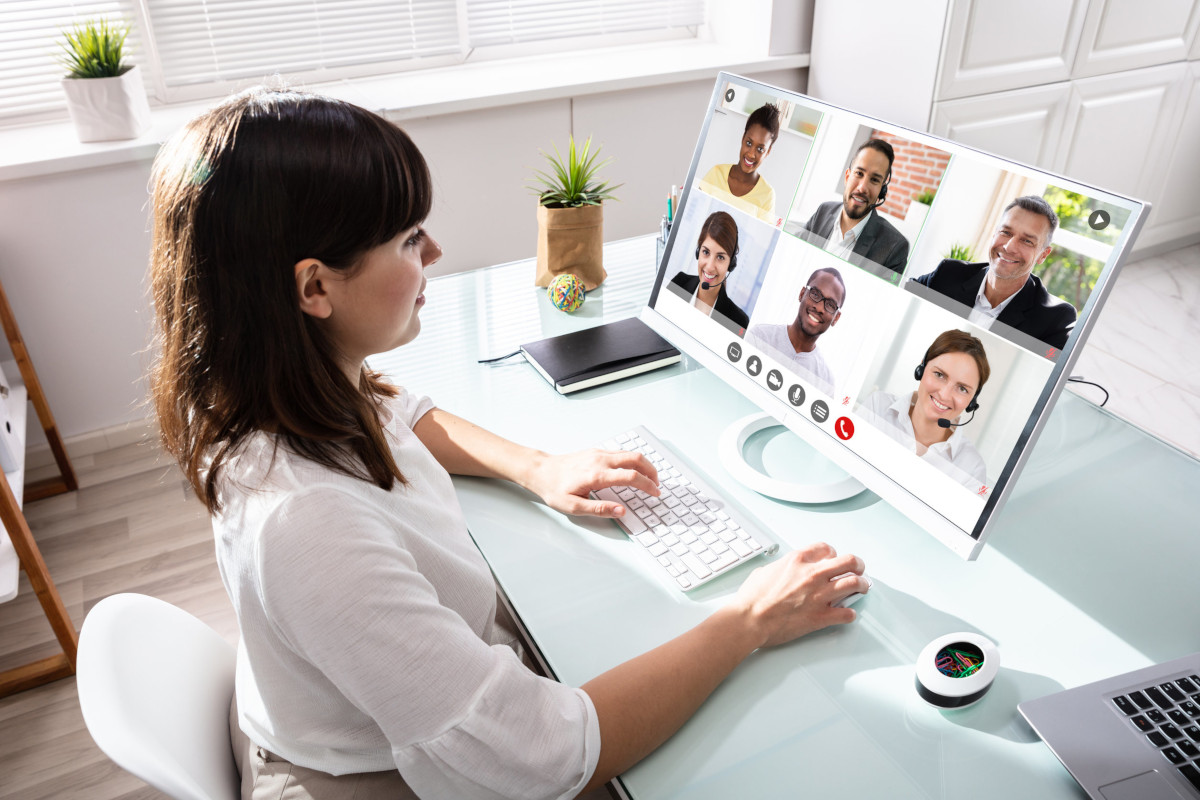 A woman working from her home office, videoconferencing on her laptop with other co-workers who are also working remotely