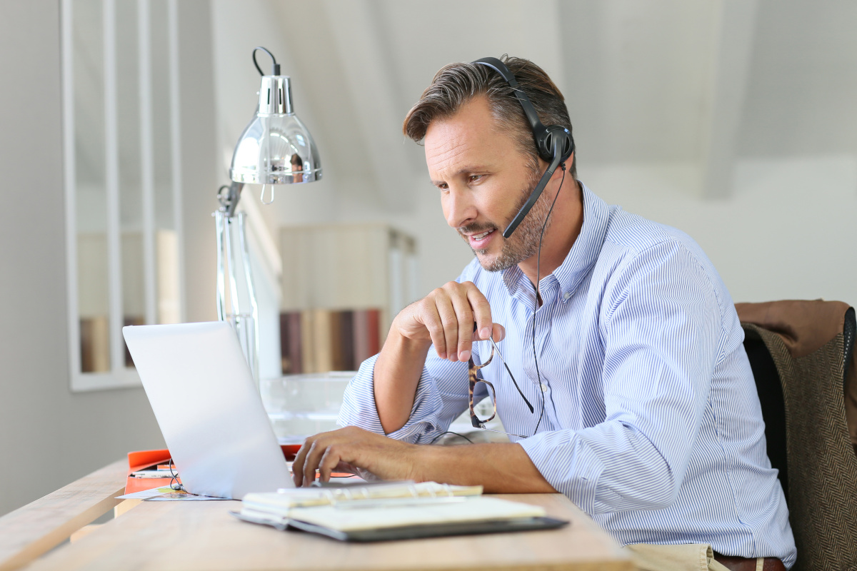 Businessman teleworking with headset and laptop computer from home office.