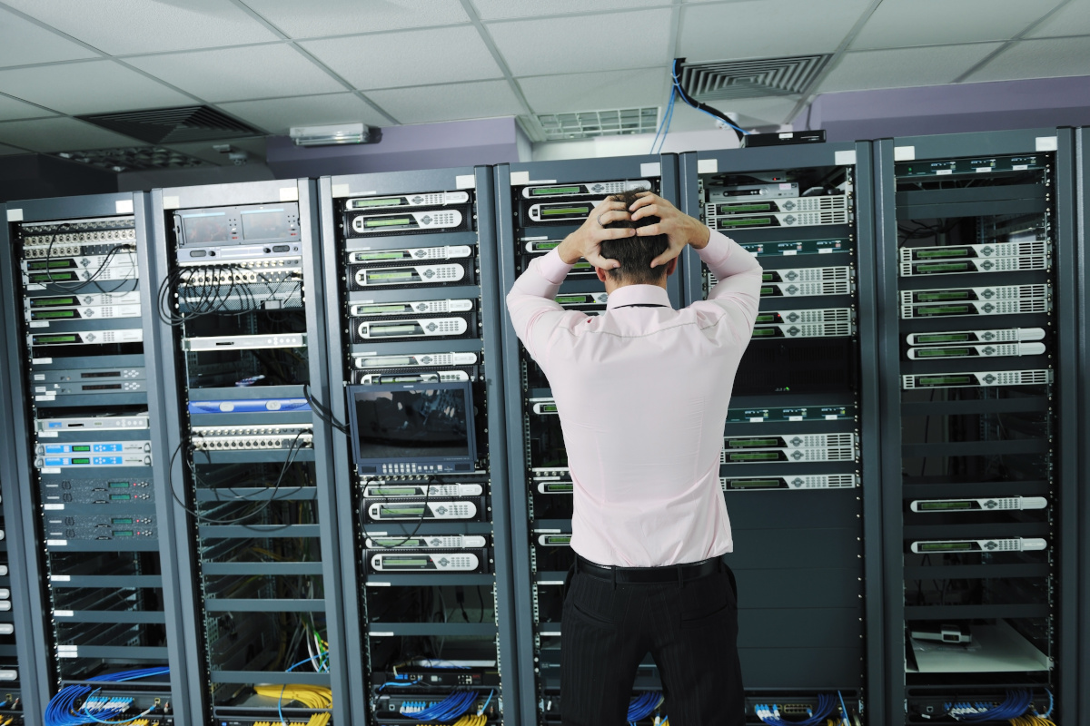 A man in dress shirt and pants grabbing the back of his head with both hands while looking at a server room after insufficient backup procedures lead to a disaster