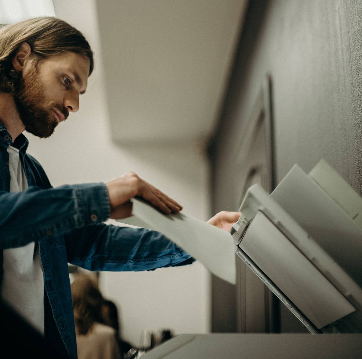 A man putting a piece of paper onto a copier while holding the lid open