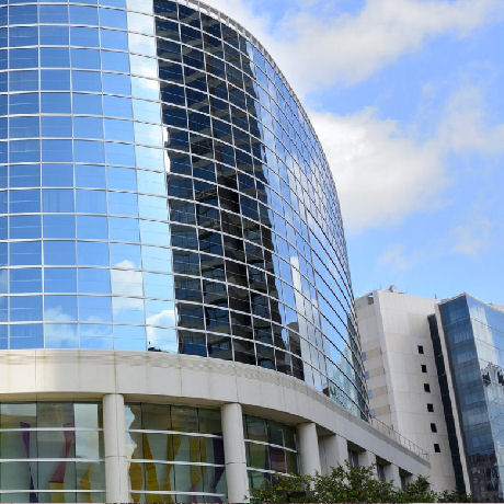 Curved highrise building with glass exterior, reflecting cloudy blue sky