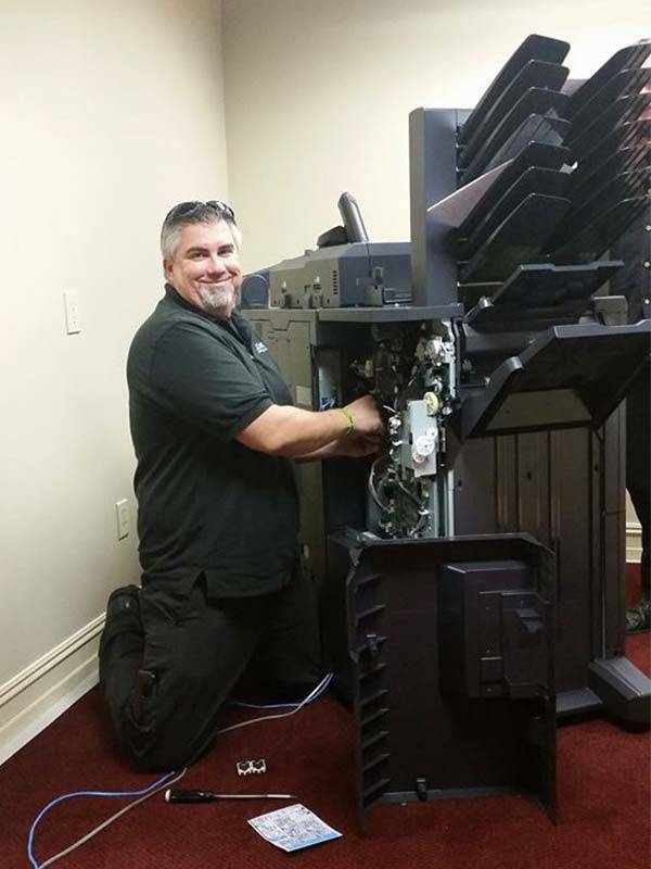 Technician smiling towards camera while working on a disassembled copier