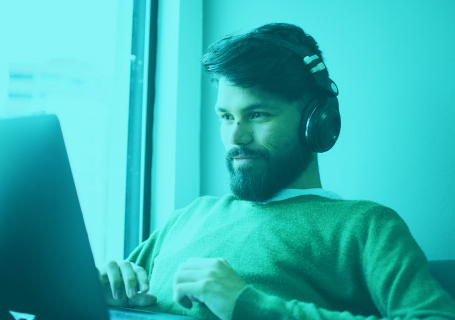 Green-hued view of bearded man wearing headphones and using a laptop