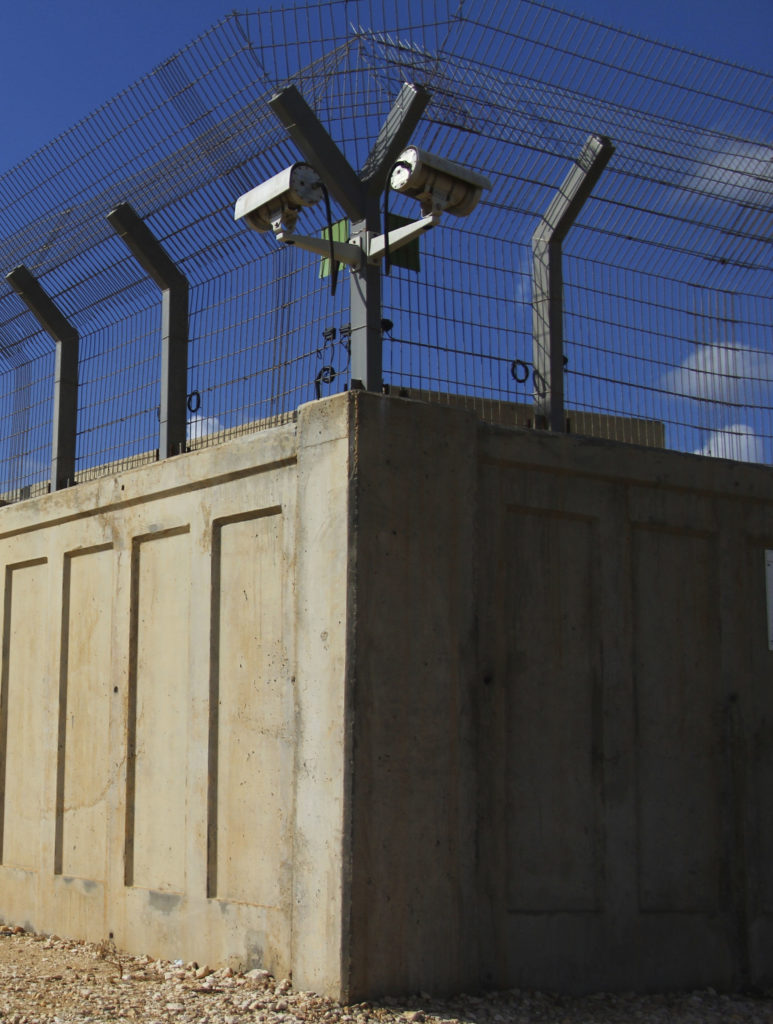 Corner of concrete fence walls with anti-climb wiring and security cameras